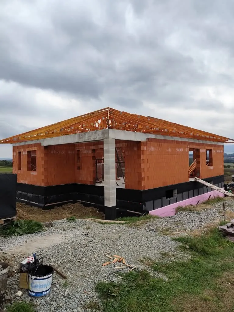 Novostavba prízemného bungalovu s murovanými stenami a čerstvo osadeným oranžovo natretým väzníkovým krovom bez krytiny